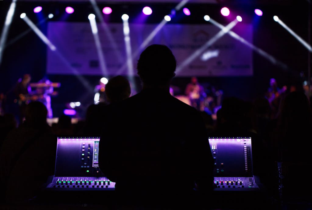A sound engineer manages the audio mixer during a vibrant live concert with colorful lighting.